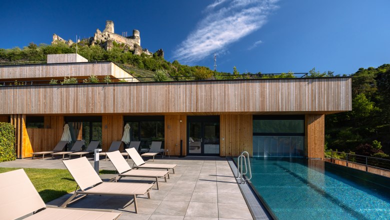 Wine Hotel Nigl, © Niederösterreich Werbung / Maximilian Pawlikowsky Modern hotel with pool and sun loungers, castle in the background.