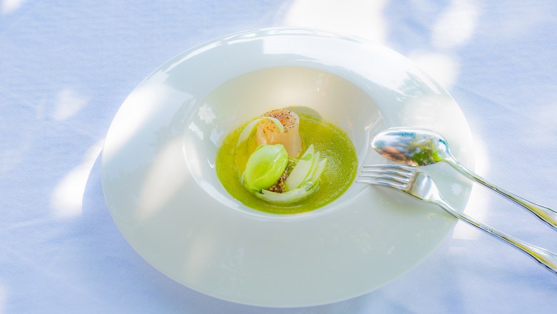 Culinary delights at the Hotel Richard Löwenherz, © Chris Saupper An elegant dish on a white plate with green sauce, a scallop and green garnish, served on a white tablecloth.