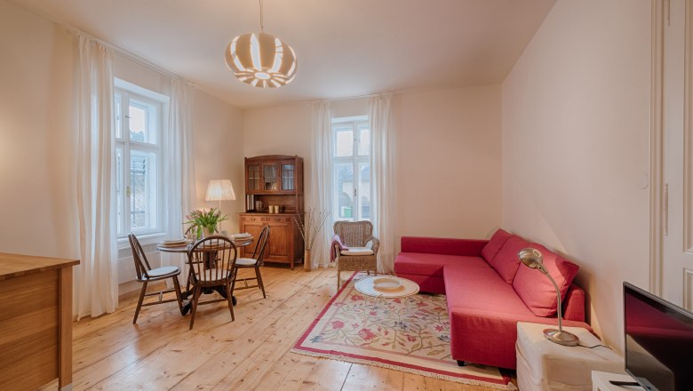 Top 2 - Living room, © VP FeWo OG Cozy living room with red sofa, wooden floor and dining table.