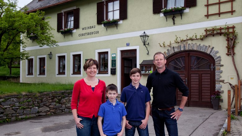 The Gebetsberger family in front of the winery, © Gebetsberger A family stands in front of a building labeled 'Weinbau Gebetsberger'.