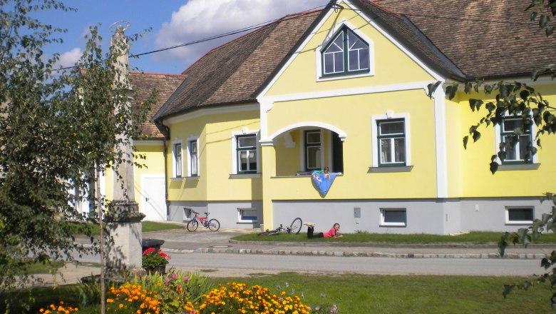 Winzerhof & Guesthouse Greil, © M. Greil Yellow guest house with flower bed and bicycles in front.