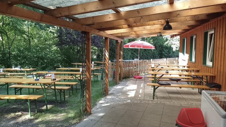 TDR-Zur MUCKE Terrace, © B.Grohotolszky Covered terrace with wooden benches and tables, surrounded by trees and a wooden fence.