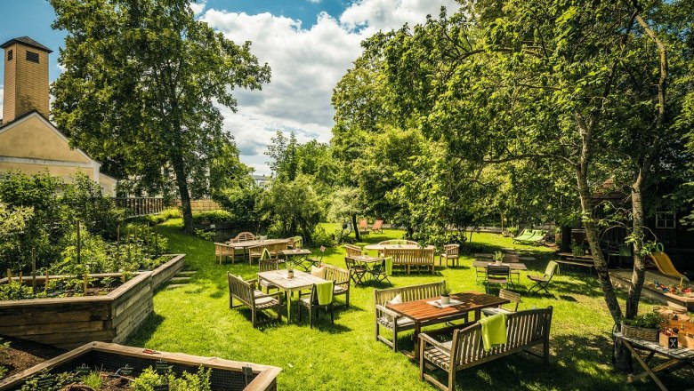 Flea Donaugartl, © Jürgen Skarwan Garden with lush greenery and wooden furniture at tables, blue sky