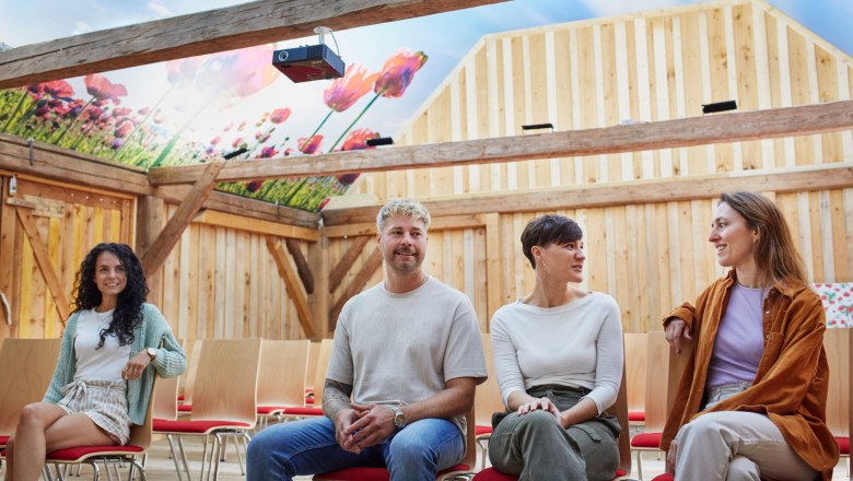Poppy farmhouse, © © Waldviertel Tourismus, Gerhard Wasserbauer Four people are sitting in a barn with a ceiling painting of poppies.