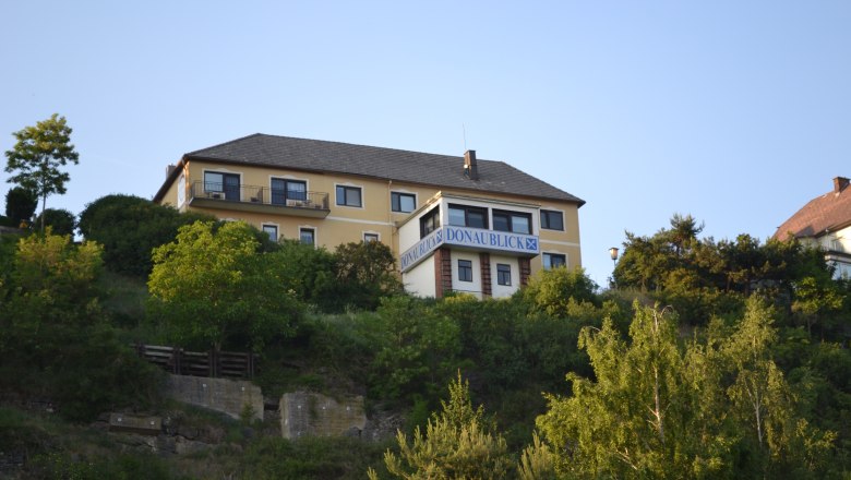 Exterior view1, © Gasthof Donaublick A yellow building with the inscription 'Donaublick' on a hill, surrounded by trees and blue sky.
