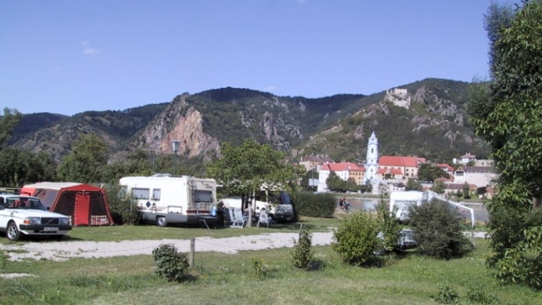 Campsite Rossatzbach, © Campingplatz Rossatzbach Campsite with caravans and tents in front of a mountain landscape and a church in the background.