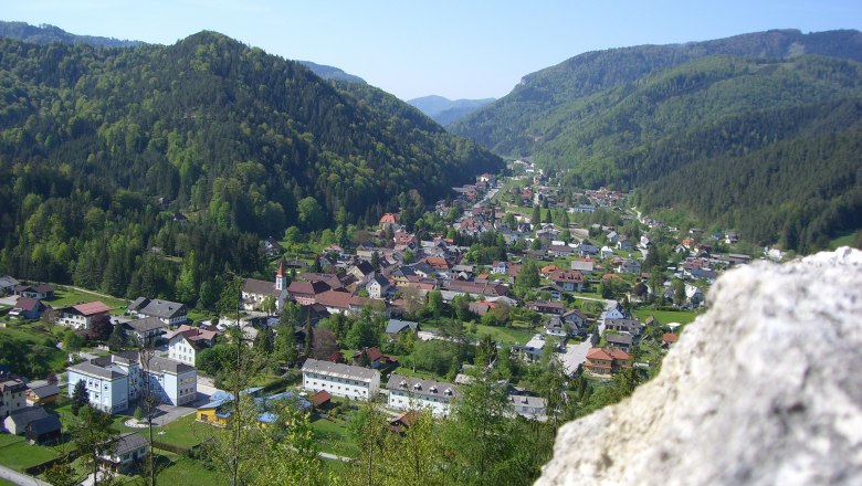 View from the castle ruins, © Gemeinde Hohenberg Panoramic view of a village in a green valley, surrounded by wooded hills, with a rock in the foreground.