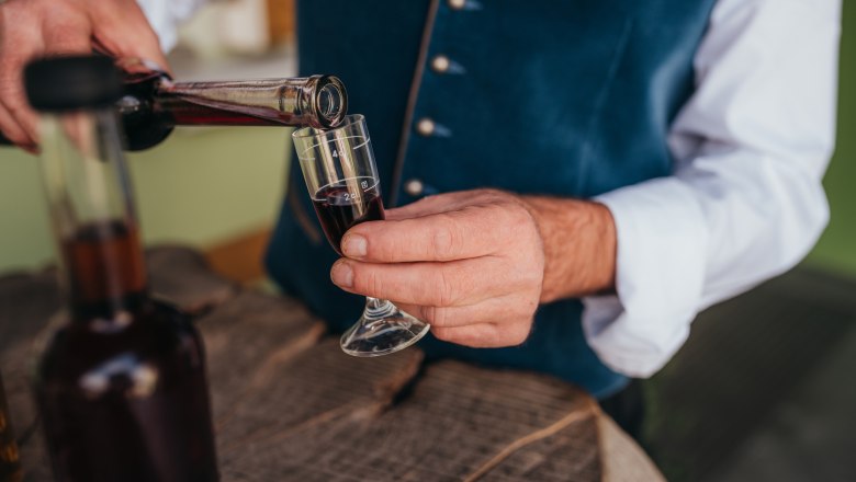 Homemade liqueurs, © Niederösterreich Werbung/Daniela Führer Person pours red liqueur into a small glass.