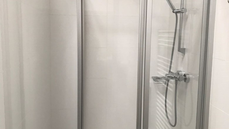 Shower in loft 2, © Konstantin Hübner Modern shower cubicle with glass walls and hand shower in a white bathroom.