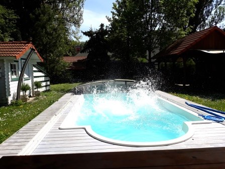 Pool, © bed and pool A pool in the garden with splashing water, surrounded by trees and a small building with a red roof.