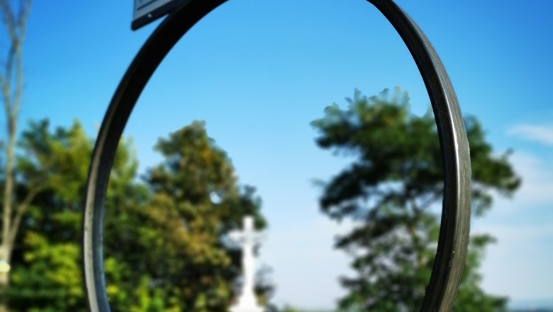 Key experience Zeißlkreuz, © Weinstraße Weinviertel A sign with the inscription 'Seefeld-Kadolz' against a blue sky, with a white cross and trees in the background.