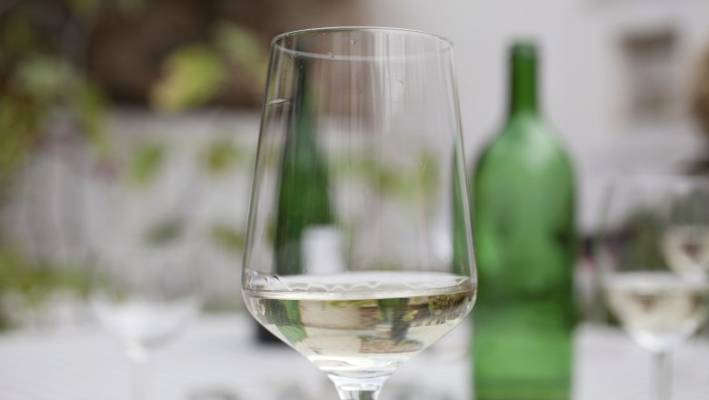 Wine glass, © Weinviertel Tourismus / Christine Wurnig A wine glass with white wine on a table, a green wine bottle in the background.