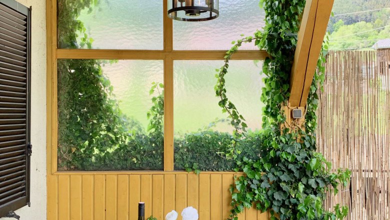 Top 1 - Terrace, © VP FeWo OG A table set on a terrace with a bottle of wine, crockery and candles, surrounded by ivy and wooden walls.