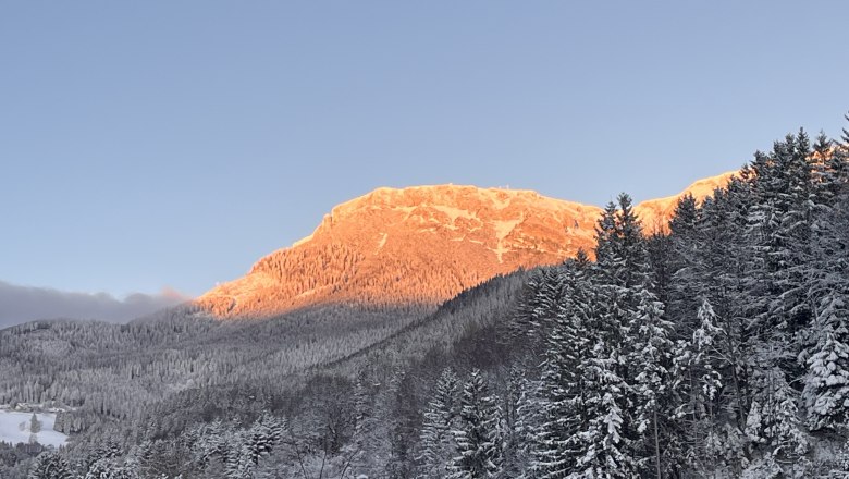 View Winter RaxChalet, © RaxChalet Snow-covered mountain landscape with orange illuminated summit at sunset.