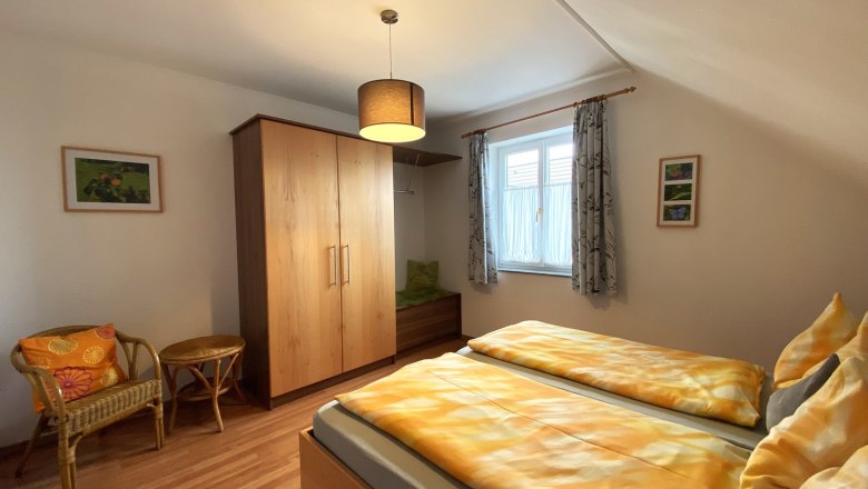 Vacation apartment Marille, © Trachsler Bedroom with double bed, wooden wardrobe, wicker chair and window with curtains.