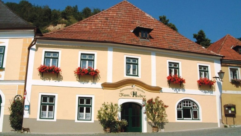 Huber winery exterior view, © Familie Huber Exterior view of a traditional building with a yellow façade and red flowers on the windows.