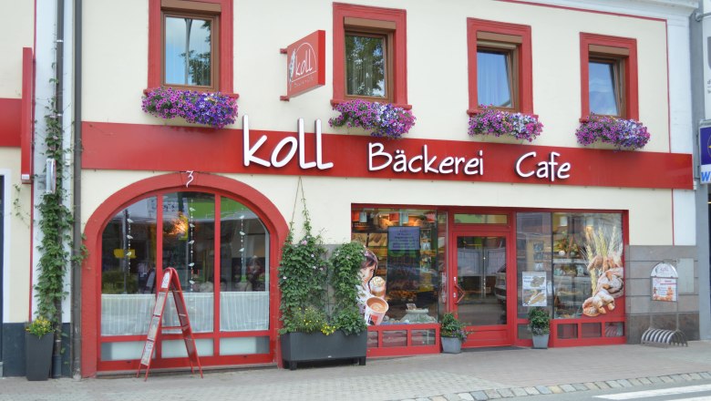 Koll Bakery Café in Kirchschlag, © Koll GmbH Exterior view of the Koll Bäckerei Café in Kirchschlag with red window frames and flower boxes.