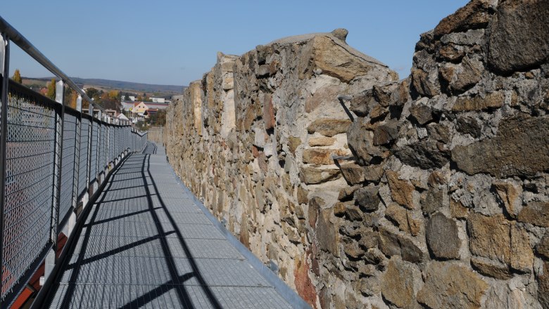 Tour of the city wall, © Veigl Harald A metal walkway along an old stone wall with a view of a town in the background.