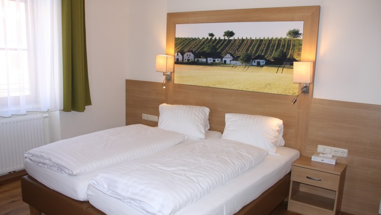Guest room, © Familie Rieder A guest room with a double bed, wooden paneling, bedside table and a picture of vineyards on the wall.