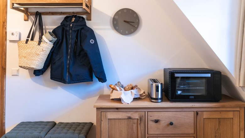 Filing, © Monika Pölzer A hallway with a wooden coat rack, a jacket, a hat, a bag, a toaster, an oven and a bread basket on a wooden cupboard.
