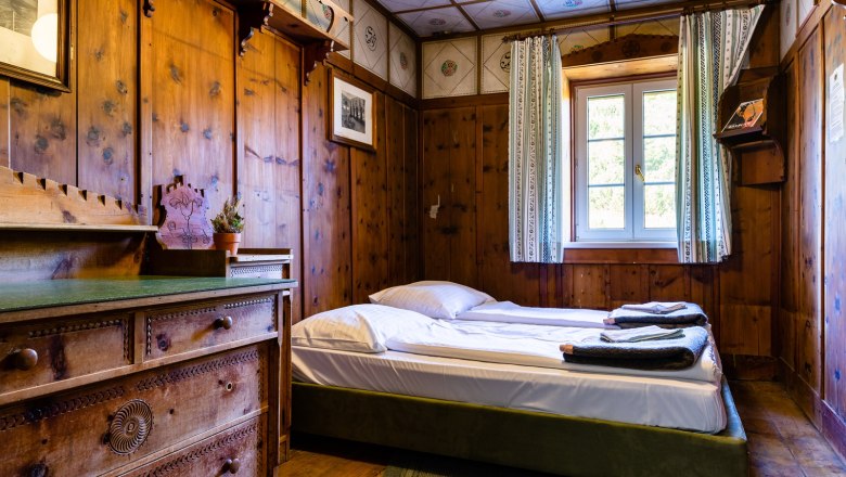 Double room, © Katrin Nusterer Rustic double room with wooden walls, a bed and a chest of drawers.