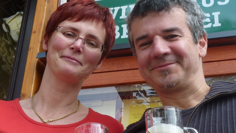 Haselböck pub brewery, © Wirtshausbrauerei Haselböck Two people clink glasses of beer in front of a sign for the Haselböck brewery.