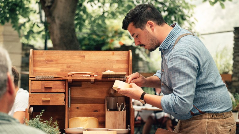 Finely composed compositions, © Hofmeisterei Hirtzberger/Julius Hirtzberger A man in a blue shirt prepares cheese on a wooden serving trolley outside.
