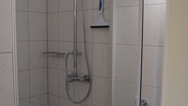 Shower, © Reep A tiled shower with shower head, shower fitting and squeegee on the wall.