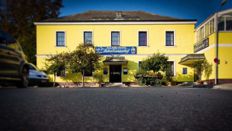 Auland-Hotel Siebenbrunnerhof, © Auland-Hotel Siebenbrunnerhof Yellow building with the inscription 'Auland-Hotel Siebenbrunnerhof', surrounded by trees and an old car.
