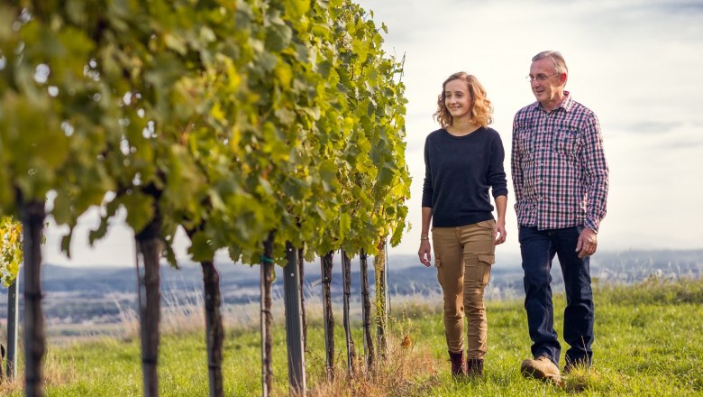 Brachmann Winery, © Weingut Brachmann Two people walking through a vineyard in sunny weather.