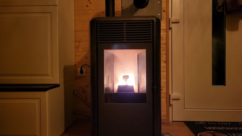 Ready for the cold season with a pellet stove and underfloor heating, © Villa to go A burning pellet stove in a room with wooden walls and a door.