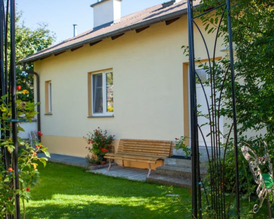 Outdoor area, © Michael Sokolar A yellow house with a garden bench and flowers in the foreground.