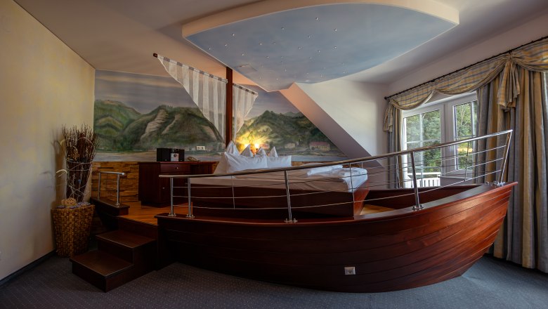 Hotel ResidenzWachau, © Niederösterreich Werbung / Maximilian Pawlikowsky Hotel room with bed in the shape of a boat, wall painting of landscape, window with curtains.