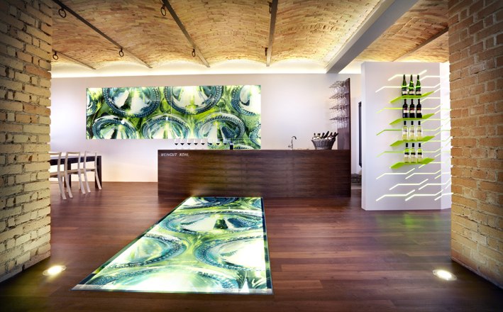 Tasting room, © Weingut Kohl Modern winery interior with illuminated floor and wine bottles on the wall.