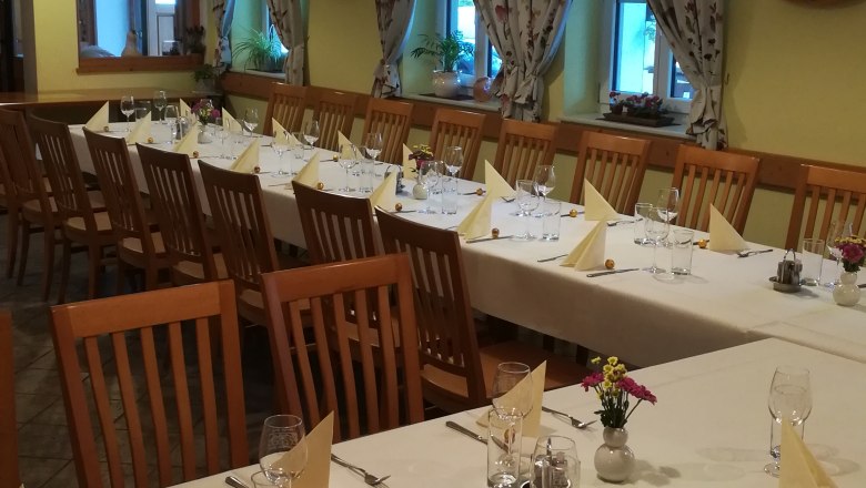 saal-family-resch, © Familie Resch A festively decorated hall with long tables, chairs and decorative curtains.