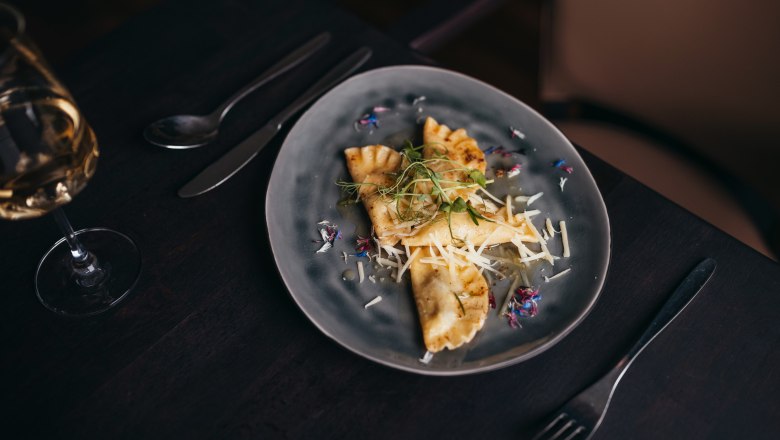 Goose ravioli in rosemary butter, © Niederösterreich Werbung/Daniela Führer Table set with filled dumplings and grated cheese on a gray plate.