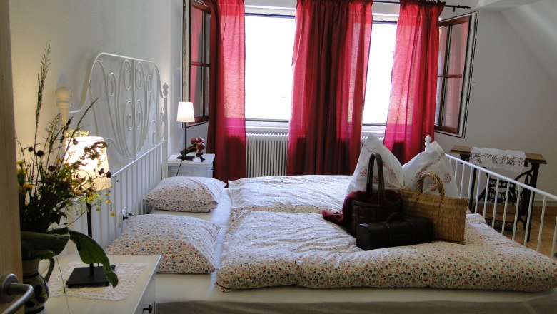 Rinntaverne, © Rinntaverne Cozy bedroom with double bed, red curtains and flowers on the bedside table.