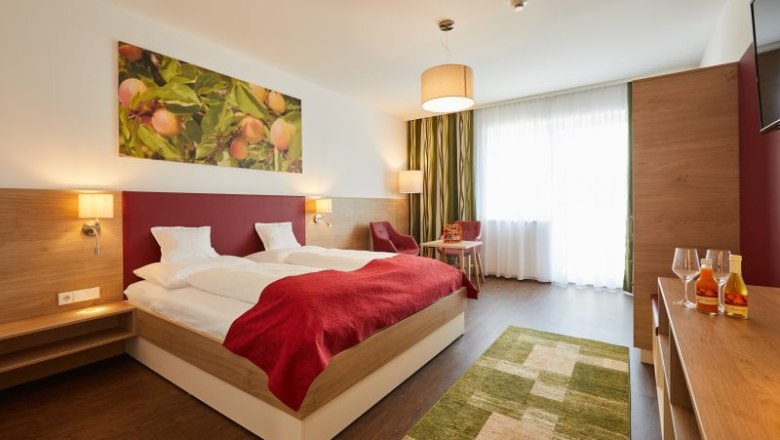 Room example at Weinhof Aufreiter, © Michael Schafranek Modern hotel room with double bed, red ceiling, wooden furniture and large window. A picture of fruit hangs on the wall.