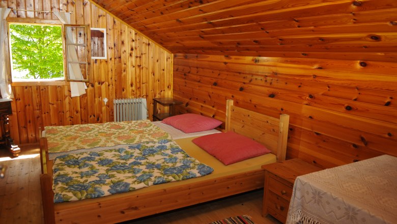 Guest house 2, © fritz fischer Wood-paneled bedroom with double bed, colorful blankets and open window.