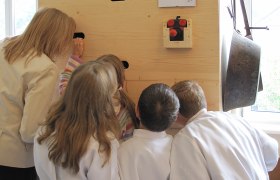 Peep box, © Herbert Bednarik Group of children and a woman looking through holes in a wooden wall.