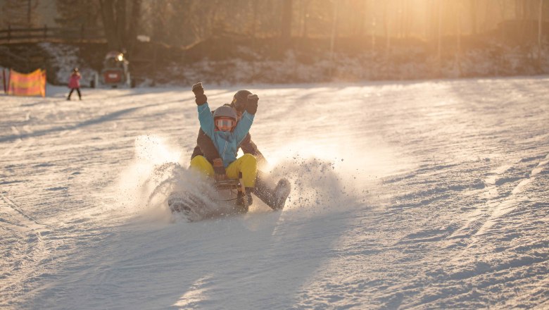 Family ski area at the Wexl Arena St. Corona am Wechsel, © Erlebnisarena St. Corona am Wechsel Two people tobogganing in the snow at sunset.