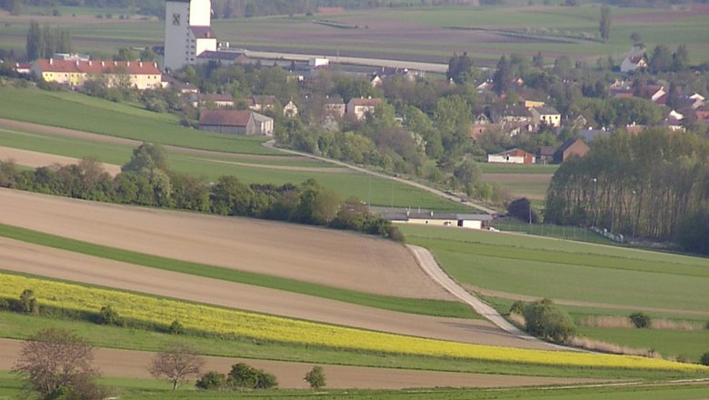 Großmugl, © Gemeinde Großmugl Landscape with fields and a village in the background, dominated by a large white building with a dark roof.