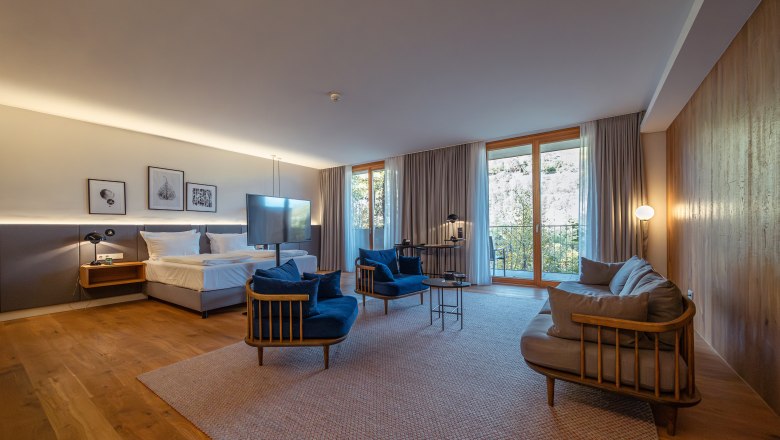 Steigenberger Hotel & Spa, Krems, © Niederösterreich Werbung/ Maximilian Pawlikowsky Modern hotel room with wooden floor, large bed, blue armchairs and large windows with curtains.