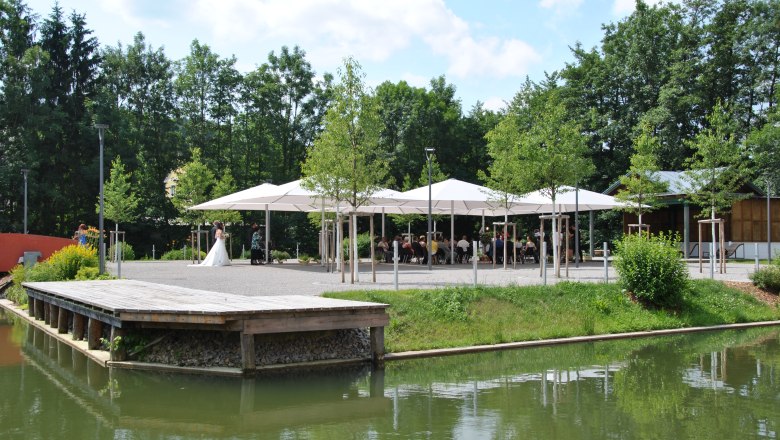 Municipality of Zeillern, © zVg Gemeinde Zeillern A wedding couple stands in front of a pavilion with guests, surrounded by trees and a pond.