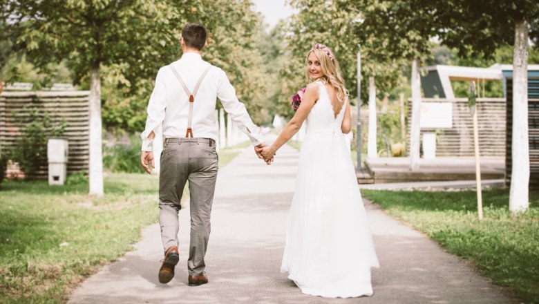 Wedding in the love garden, DIE GARTEN TULLN, © Klaus Bauer A bride and groom walk hand in hand along a path in the garden, the bride smiles back.