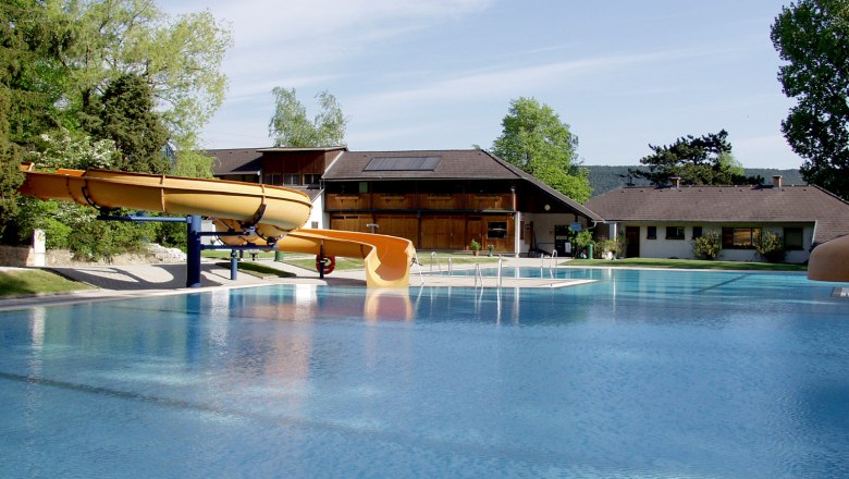 Waldbad Markt Piesting, © Isabella Palfy An outdoor pool with slide and buildings in the background.