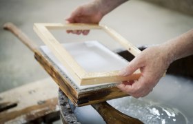 paper mill_02, © Waldviertel Tourismus, Robert Herbst Close-up of hands holding a wooden frame over a paper pulp in a traditional paper mill.