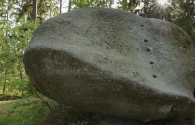 Wobbling stone near Amaliendorf, © Matthias Schickhofer A large, oval boulder in the forest with sunbeams in the background.