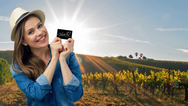 VinoQ, © ohida OG / ohne.media Woman with hat holding VinoQ card in front of a sunny vineyard.