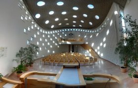 Interior, © Evangelische Gemeinde Klosterneuburg Modern church interior with round windows and wooden furniture.